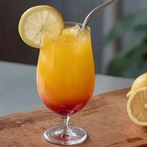 Cocktail Bora Bora sans alcool au dégradé rouge et orange, garni d’une rondelle de citron, servi frais avec une paille.