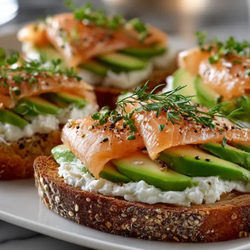 Tartine avocat saumon servie sur pain croustillant avec fromage frais, tranches d’avocat et saumon fumé, garnie d’herbes fraîches.
