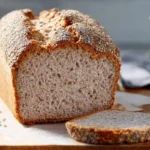 Pain au sarrasin sans gluten maison, à la croûte dorée et mie moelleuse, posé sur une planche de bois avec une tranche tranchée.