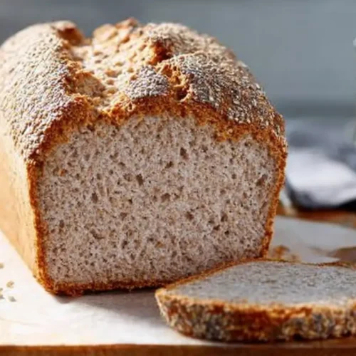 Pain au sarrasin sans gluten maison, à la croûte dorée et mie moelleuse, posé sur une planche de bois avec une tranche tranchée.