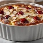 Clafoutis sans gluten doré et moelleux, garni de cerises fraîches et d’amandes effilées, dans un plat en céramique blanc prêt à être dégusté.
