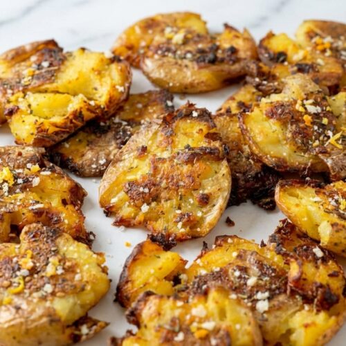Vue de dessus de la recette smashed potatoes ultra croustillantes sur marbre blanc, assaisonnées au sel d'agrumes et zaatar.