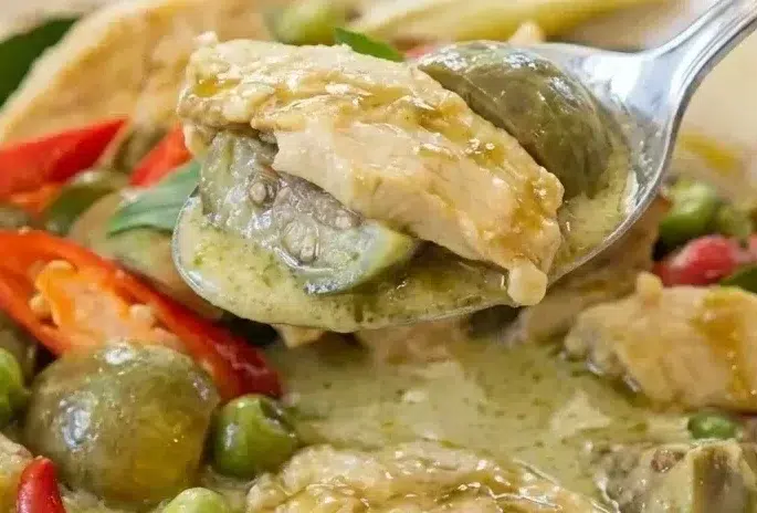 Curry vert au poulet onctueux infusé au galanga, servi dans un bol minimaliste sur un plan de travail en marbre.