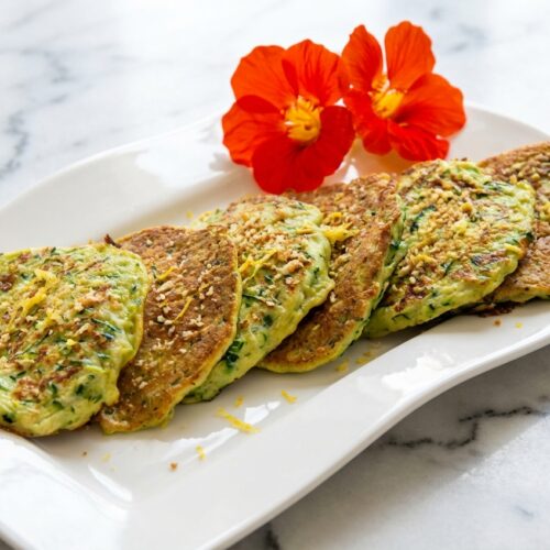 Galette de courgettes dorée à la chapelure Panko croustillante et zestes de citron sur marbre blanc en lumière naturelle.