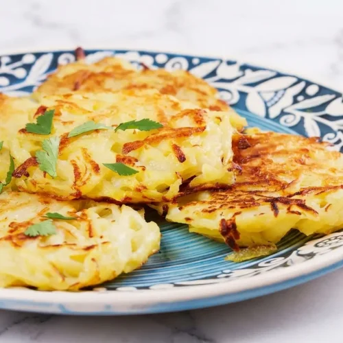 Crêpes de pommes de terre dorées, texture aérée par la crème et la levure, sur céramique blanche et marbre.