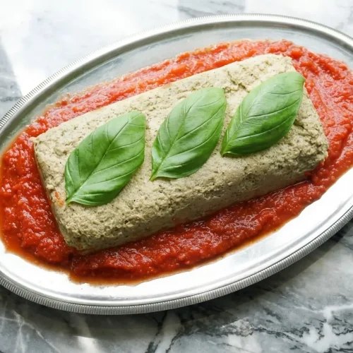 Pain d'aubergine fondant à la poudre de noisettes et cumin sur marbre blanc en lumière naturelle.