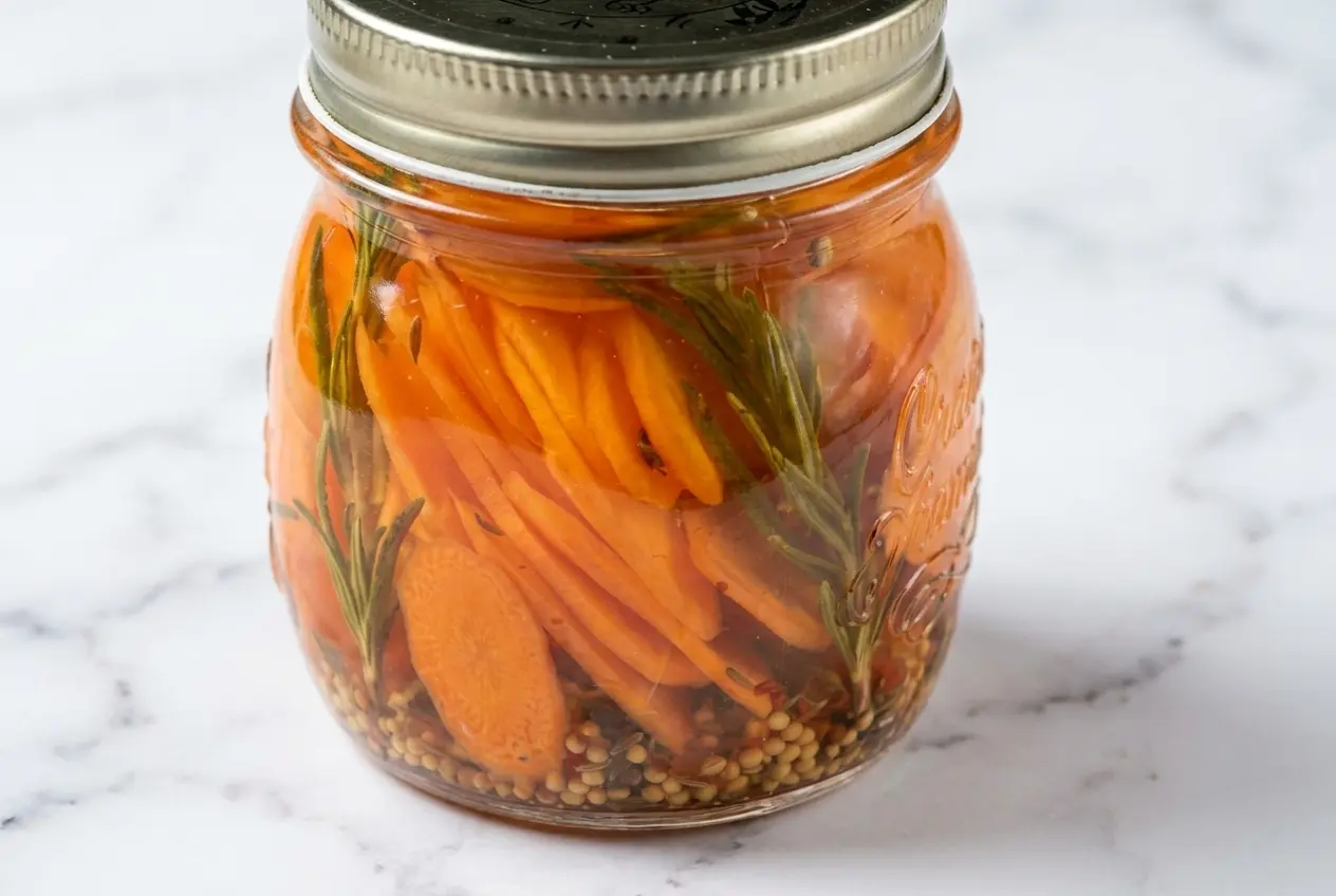 Pickles de carottes dans un bol minimaliste sur marbre blanc. Saumure infusée aux épices torréfiées sous lumière naturelle.