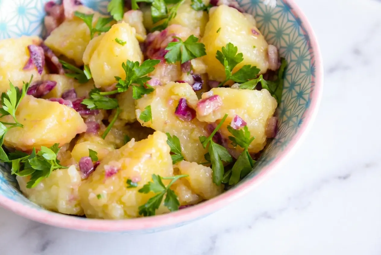 Pommes de terre vinaigrette déglacées au vin blanc sec, présentées dans un bol en céramique sur un marbre blanc.
