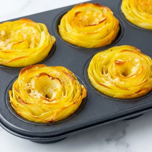 Rosace de pomme de terre croustillante au beurre noisette et romarin, présentée sur une assiette en céramique minimaliste au centre d'un comptoir en marbre blanc sous une douce lumière naturelle.