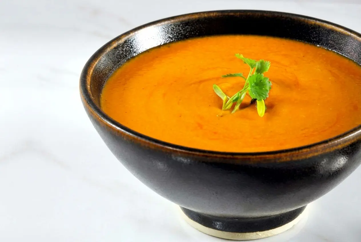 Velouté de carottes et poivrons aux zestes d'orange et piment d'Espelette dans un bol en céramique blanc minimaliste.