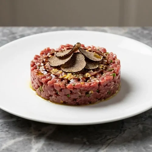 Tartare de veau à la truffe dressé en cercle sur une assiette en céramique, rehaussé de jaune d'œuf confit haché, sur un comptoir en marbre avec éclairage de fenêtre.
