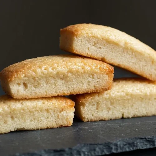 Pile de financiers aux amandes, dorés et moelleux, sur une assiette foncée.