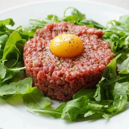Recette steak tartare classique servi dans une assiette blanche, garni d'un jaune d'œuf cru au centre, avec une texture fraîche et fondante.