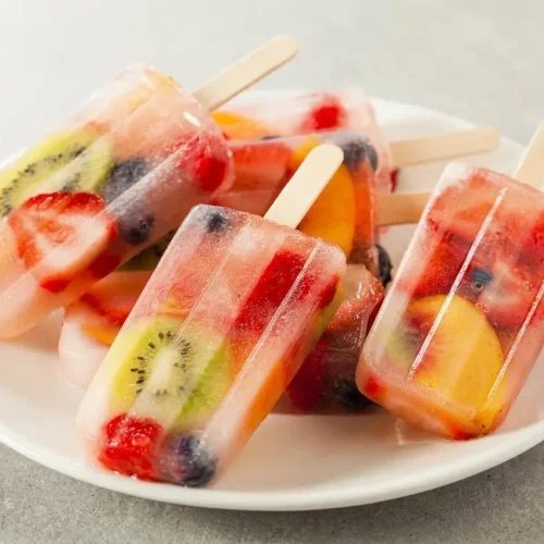 Quatre glaces à l'eau aux fruits rouges dans leur moule en céramique blanc, l'une d'elles est soulevée, montrant sa texture glacée.