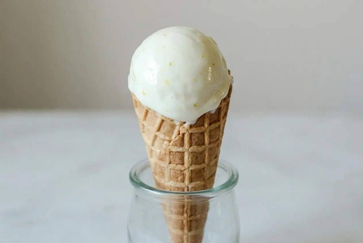 Glace au citron crémeuse servie dans un bac en céramique blanc, avec des boules déjà formées et des tranches de citron frais.