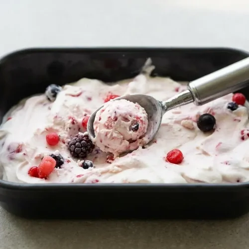 Glace au yaourt sans sorbetière onctueuse aux fruits rouges, présentée dans un plat à cake blanc sur un fond sombre.