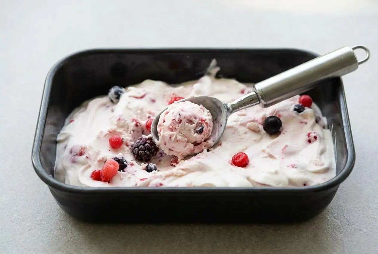 Glace au yaourt sans sorbetière onctueuse aux fruits rouges, présentée dans un plat à cake blanc sur un fond sombre.