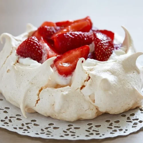 Pavlova aux fraises entière sur un plat de service, garnie de crème chantilly, de fraises fraîches et nappée d'une gelée brillante.