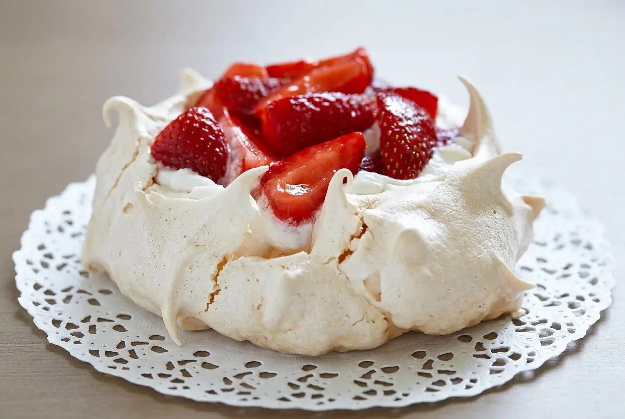 Pavlova aux fraises entière sur un plat de service, garnie de crème chantilly, de fraises fraîches et nappée d'une gelée brillante.