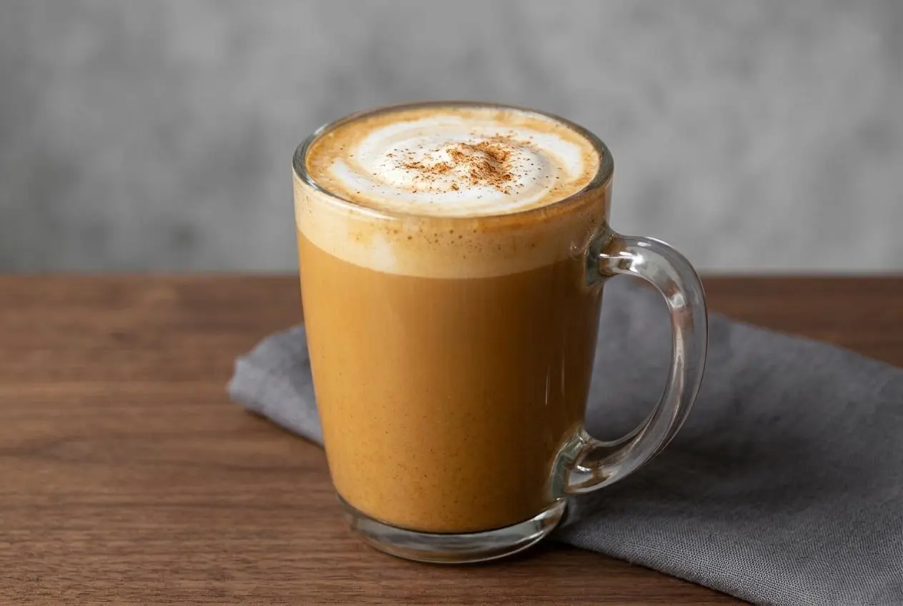 Recette Pumpkin spice latte maison dans une tasse en verre, garni de crème fouettée onctueuse et d'un saupoudrage d'épices.