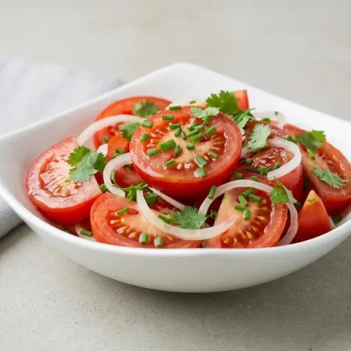 Salade de tomates fraîche dans un saladier blanc, avec des quartiers de tomates juteuses, de l'oignon émincé et des herbes fraîches.