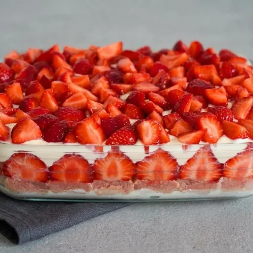 Tiramisu aux fraises dans un grand plat en verre, montrant ses couches crémeuses et son dessus décoré de fraises fraîches coupées.