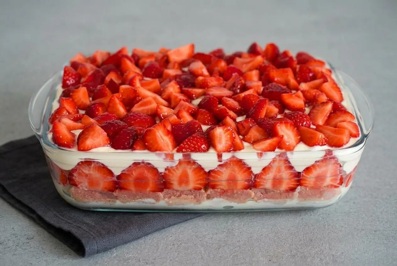 Tiramisu aux fraises dans un grand plat en verre, montrant ses couches crémeuses et son dessus décoré de fraises fraîches coupées.