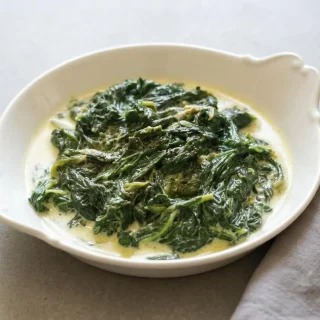 Poêlée d'épinards frais à la moutarde de Dijon et à la crème liquide dans un bol en céramique.
