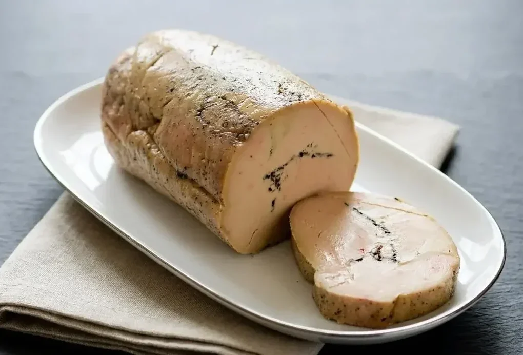 Terrine de foie gras aux truffes coupée en tranches épaisses dévoilant un marbrage de brisures de truffe noire
