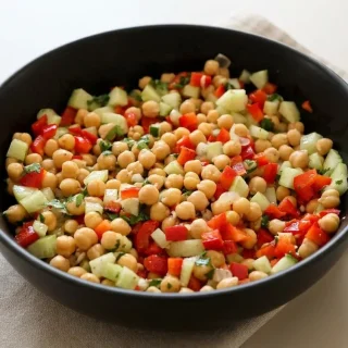 Salade de pois chiches fraîche avec poivron rouge et concombre assaisonnée de citron et coriandre dans un bol blanc.