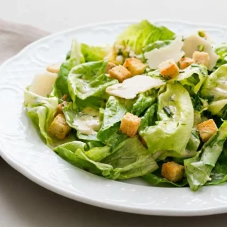 Salade César fraîche avec feuilles de romaine, croûtons dorés et copeaux de parmesan nappés de sauce crémeuse.