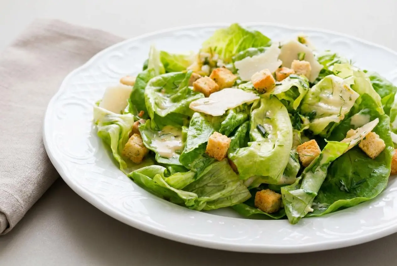 Salade César fraîche avec feuilles de romaine, croûtons dorés et copeaux de parmesan nappés de sauce crémeuse.