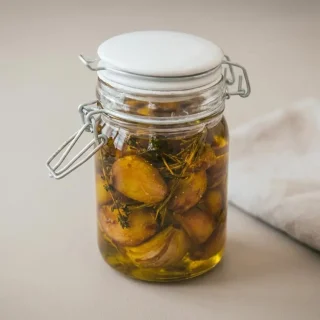 Gousses d'ail confit au four dorées et fondantes baignant dans une huile d'olive brillante aux herbes.