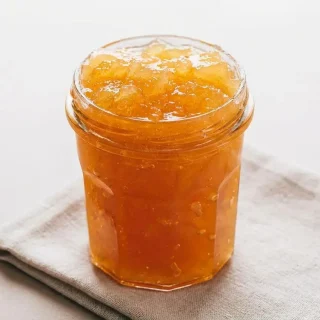 Confiture de pommes maison aux morceaux fondants et translucides dans un bocal en verre.