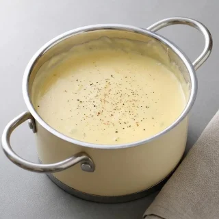 Sauce mornay dorée et onctueuse servie dans un saucier en céramique.