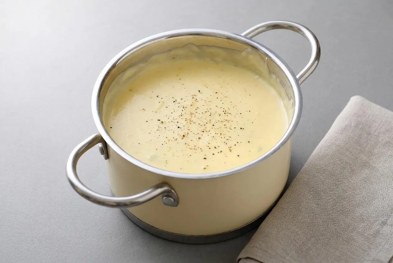 Sauce mornay dorée et onctueuse servie dans un saucier en céramique.