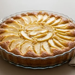 Tarte suisse aux pommes dorée au four et saupoudrée de sucre glace sur plat de service.