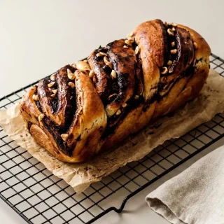 Babka au chocolat dorée et moelleuse, marbrée d'une garniture fondante et parsemée de noisettes torréfiées.