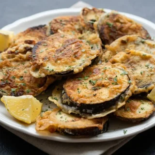 Beignets d’aubergines dorés et croustillants servis sur un plat avec des quartiers de citron et du persil frais