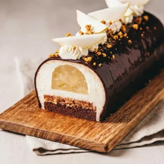 Bûche poire chocolat entière nappée d'un glaçage miroir cacao brillant sur son plat de service