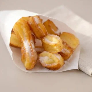 Bâtonnets de churros maison dorés et croustillants saupoudrés de sucre fin.