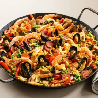Recette paella traditionnelle garnie de crevettes, moules et riz safrané au reflet doré.