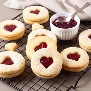 Sablés à la confiture aux amandes poudrés de sucre glace avec un cœur brillant aux fruits rouges